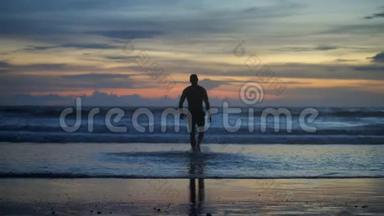 英俊的肌肉男在夕阳下走向海浪的剪影